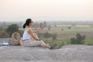 young-woman-sitting-with-mobile-phone-high-mountains-tourist-path-sunset_1150-42459